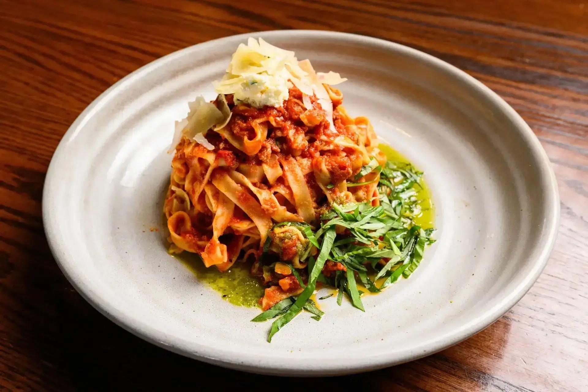 Premium Italian tagliatelle pasta with rich meat ragu sauce, served alongside fresh green pesto and topped with ricotta and shaved parmesan cheese.