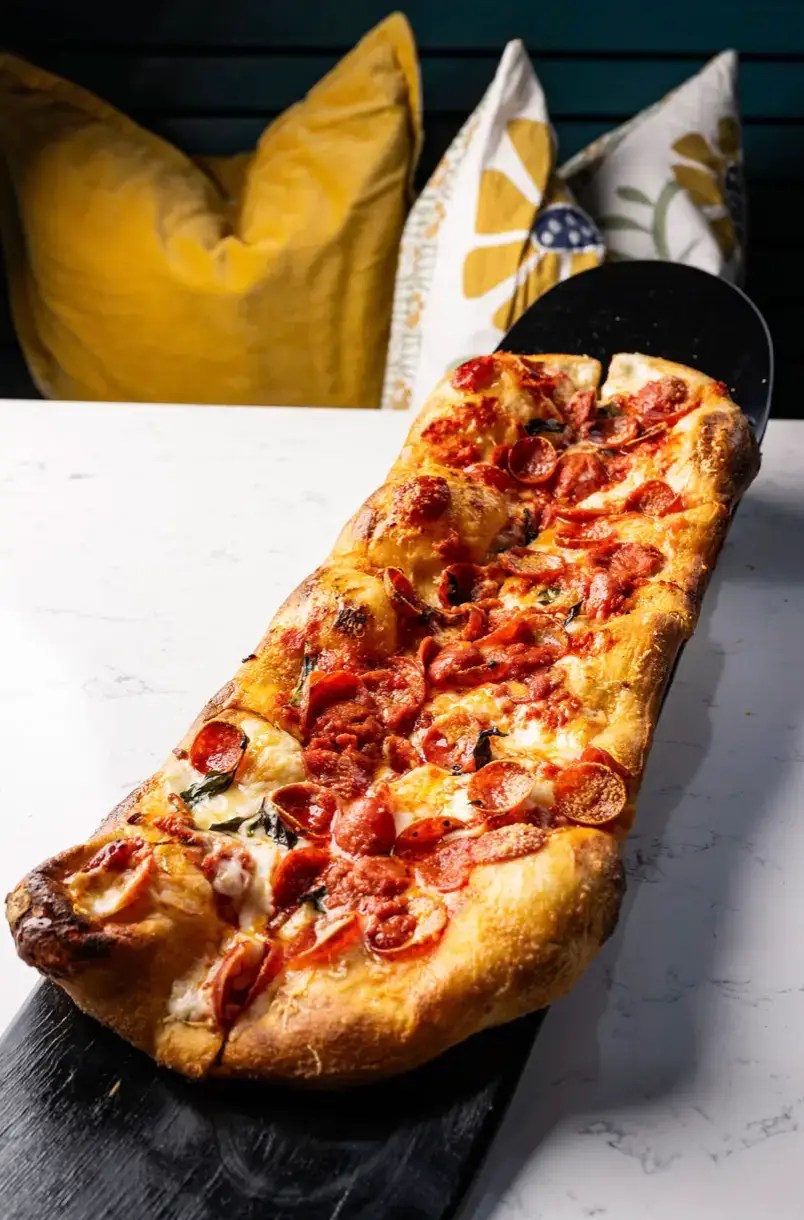 Freshly baked pepperoni flatbread pizza with melted cheese and fresh basil on a black serving platter over a white marble table.